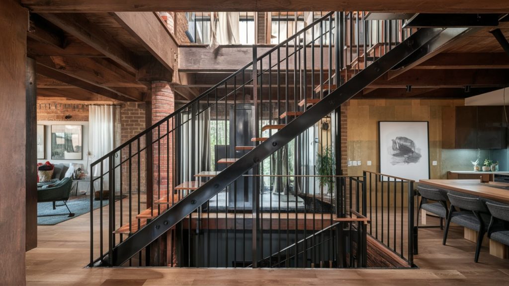 A sleek, black metal staircase with open treads and a wooden handrail, leading to a second-floor landing.