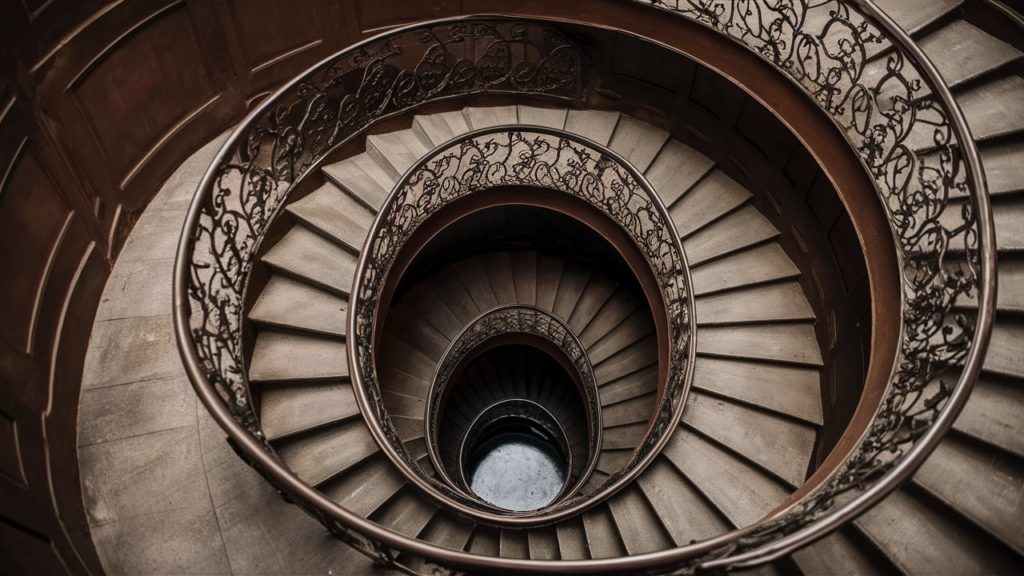 A spiral staircase with intricate wrought iron railings and a stone floor