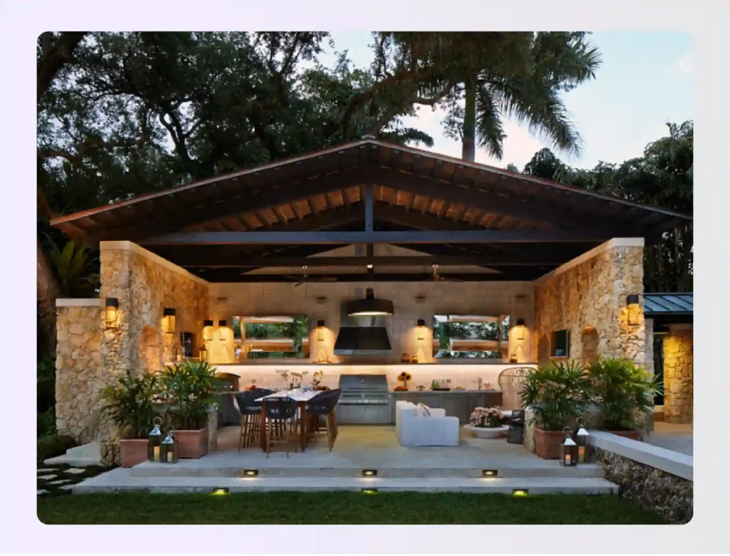 Covered outdoor pavilion with kitchen, dining table, and stone walls