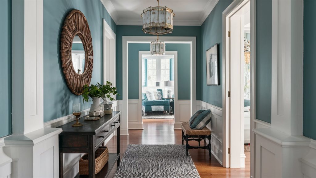 A hallway with periwinkle blue walls, white trim, and a woven mirror.