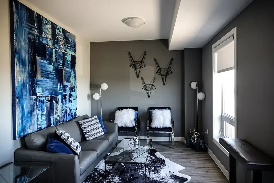 A modern living room with a large abstract painting, geometric wall decor, and a cowhide rug.