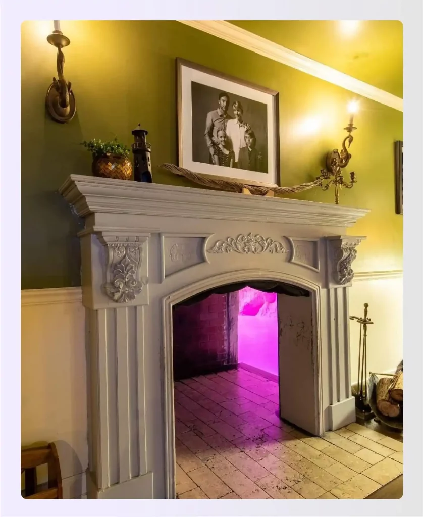 A white fireplace mantel with an opening to a pink-lit room