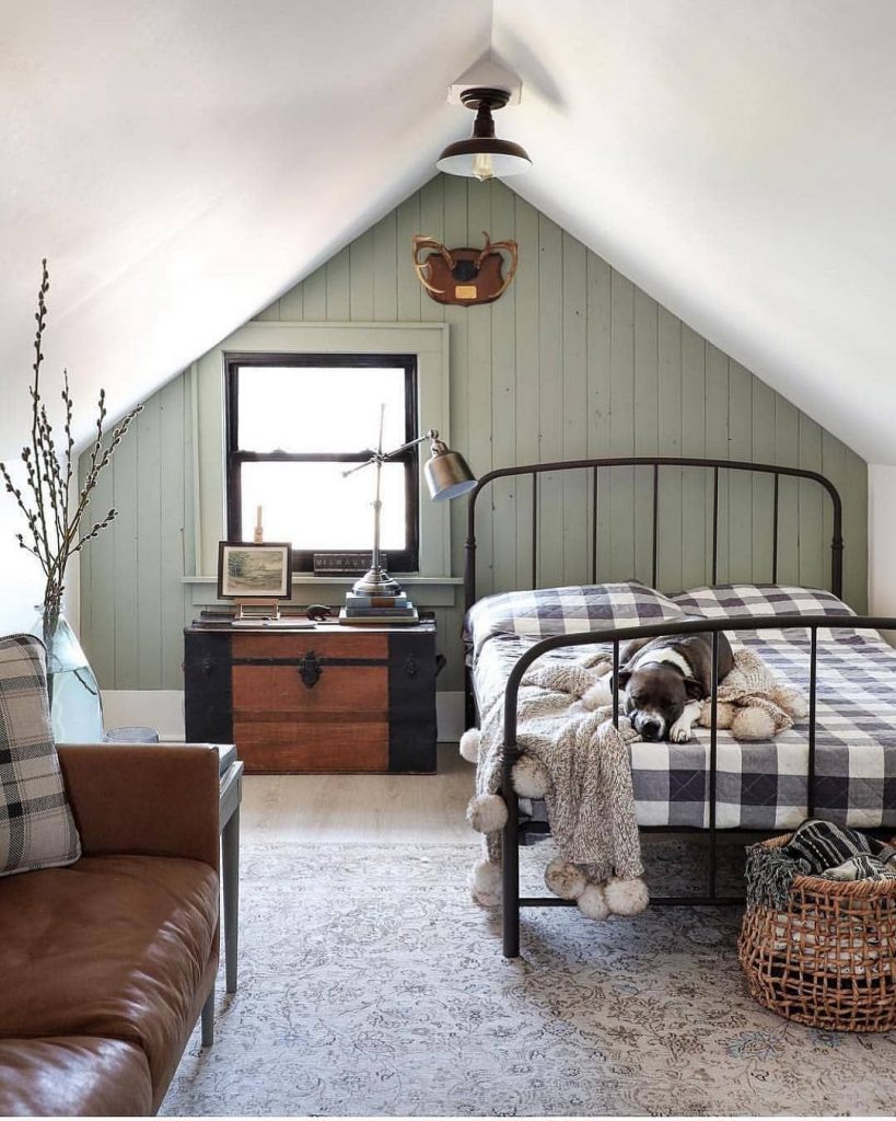 A cozy attic bedroom with a metal bed frame, plaid bedding, and a leather armchair.
