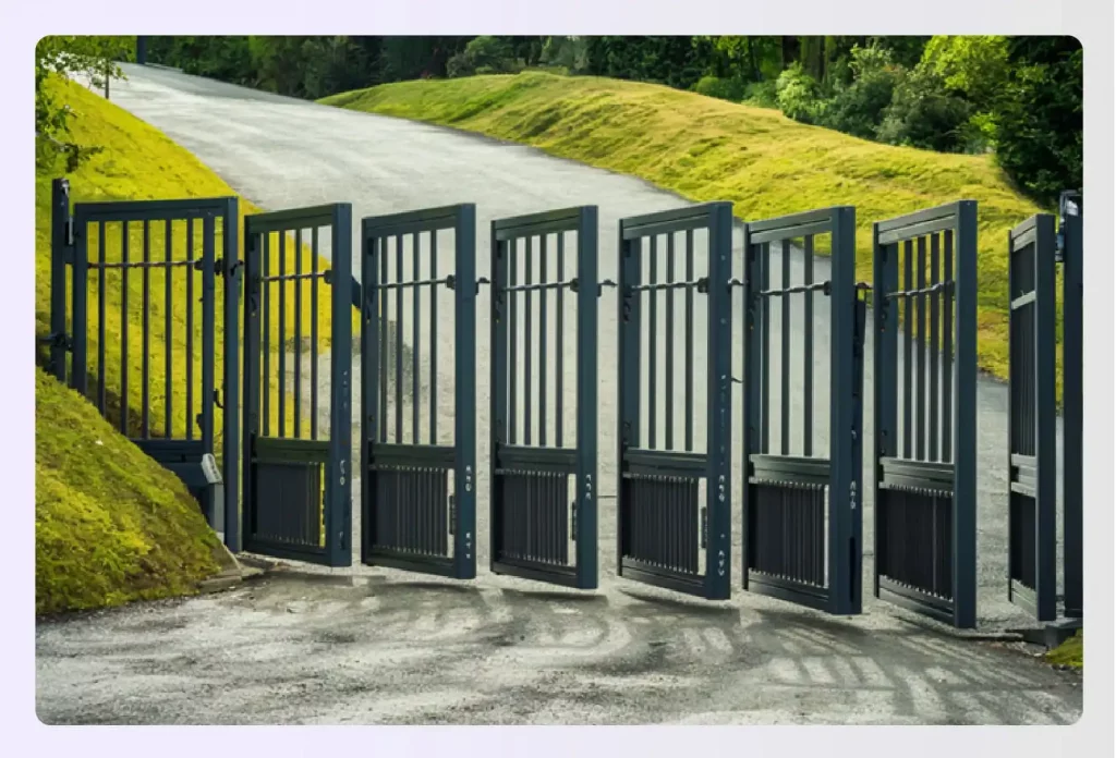 A black bi-folding gate opening on a sloped driveway