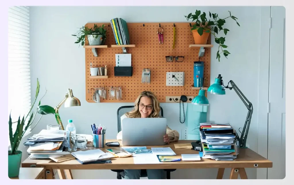 A cluttered desk with a pegboard organizer on the wall A cluttered desk with a pegboard organizer on the wall