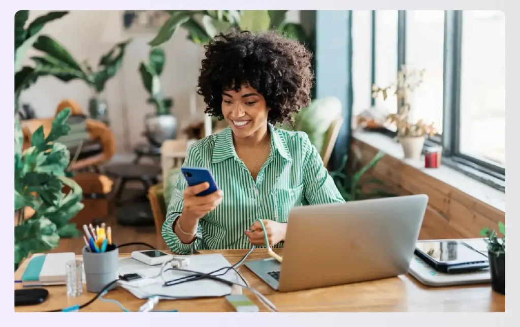 A smiling woman at her desk with multiple devices A smiling woman at her desk with multiple devices